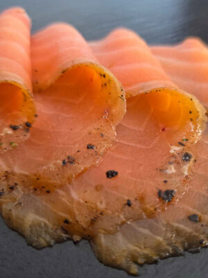 Espresso-Lachs mit dunklem Gewürzrand in dünnen Scheiben auf Schieferplatte angerichtet.