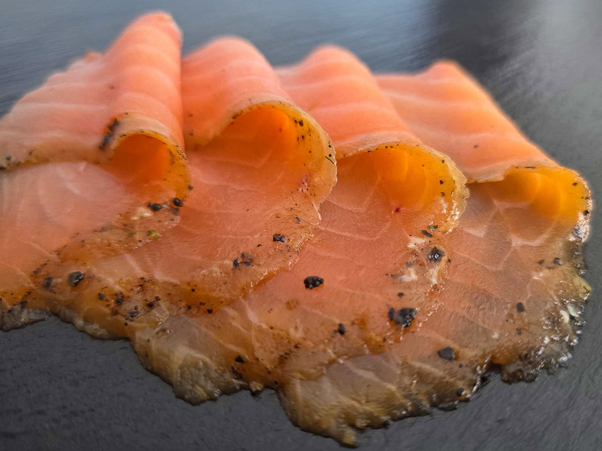 Espresso-Lachs mit dunklem Gewürzrand in dünnen Scheiben auf Schieferplatte angerichtet.