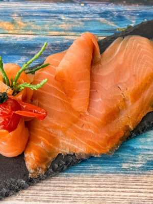 Irischer Wildräucherlachs in feinen Scheiben auf Schieferplatte mit Zitronenspalten angerichtet.