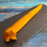 Heißgeräucherte Schillerlocken aus Dornhai auf dunkler Platte, goldgelb geräuchert, angerichtet mit Tomaten und Kräutern