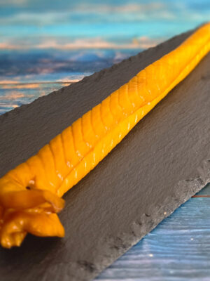 Heißgeräucherte Schillerlocken aus Dornhai auf dunkler Platte, goldgelb geräuchert, angerichtet mit Tomaten und Kräutern