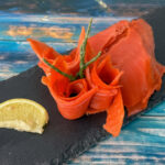 Sockeye-Alaska-Wildräucherlachs mit kräftig roter Farbe, angerichtet auf Schieferplatte mit Zitronenspalte.