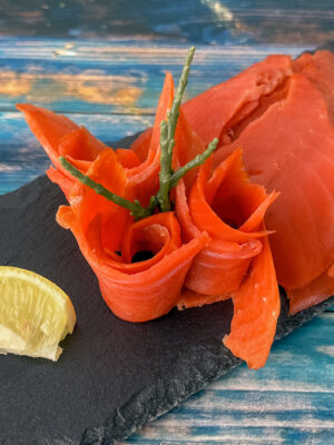 Sockeye-Alaska-Wildräucherlachs mit kräftig roter Farbe, angerichtet auf Schieferplatte mit Zitronenspalte.
